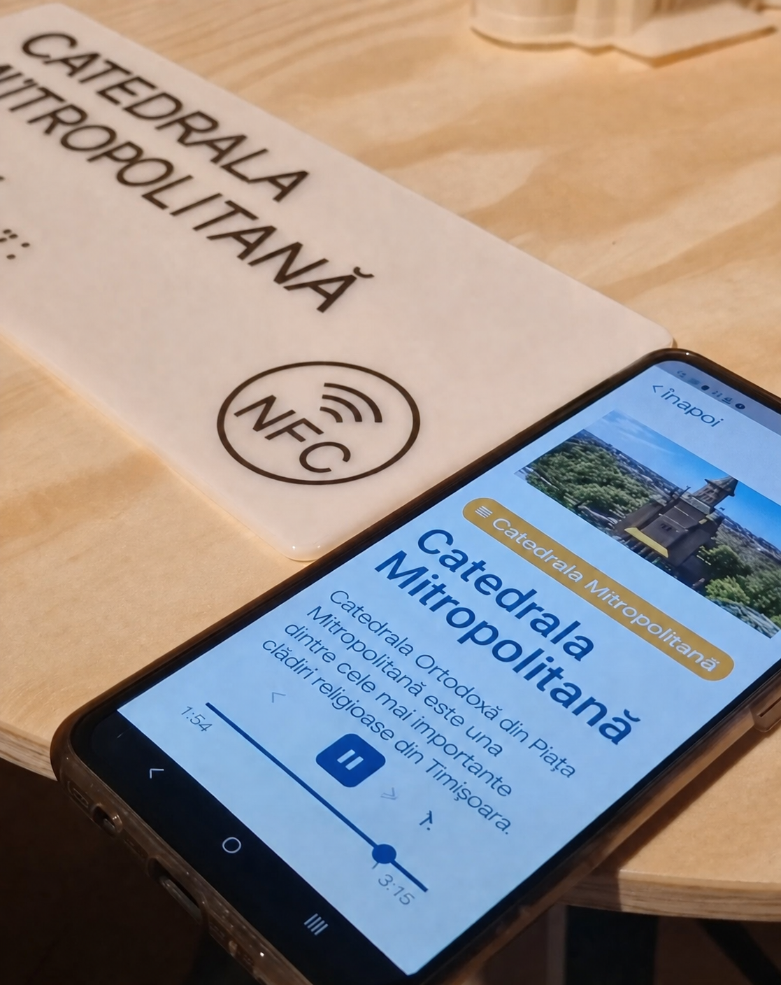 Telefon mobil apropiat de o etichetă NFC amplasată pe o machetă tactilă a Catedralei Mitropolitane. Pe ecranul telefonului este afișată aplicația ArtEcho, care redă informații despre obiectul cultural prin intermediul unui ghid multimedia accesibil.